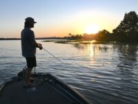Angler casting fishing rig across shallow open water flats at sunrise