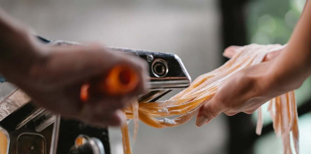Happy family enjoying fresh homemade tagliatelle made with electric motor pasta roller at dinner table