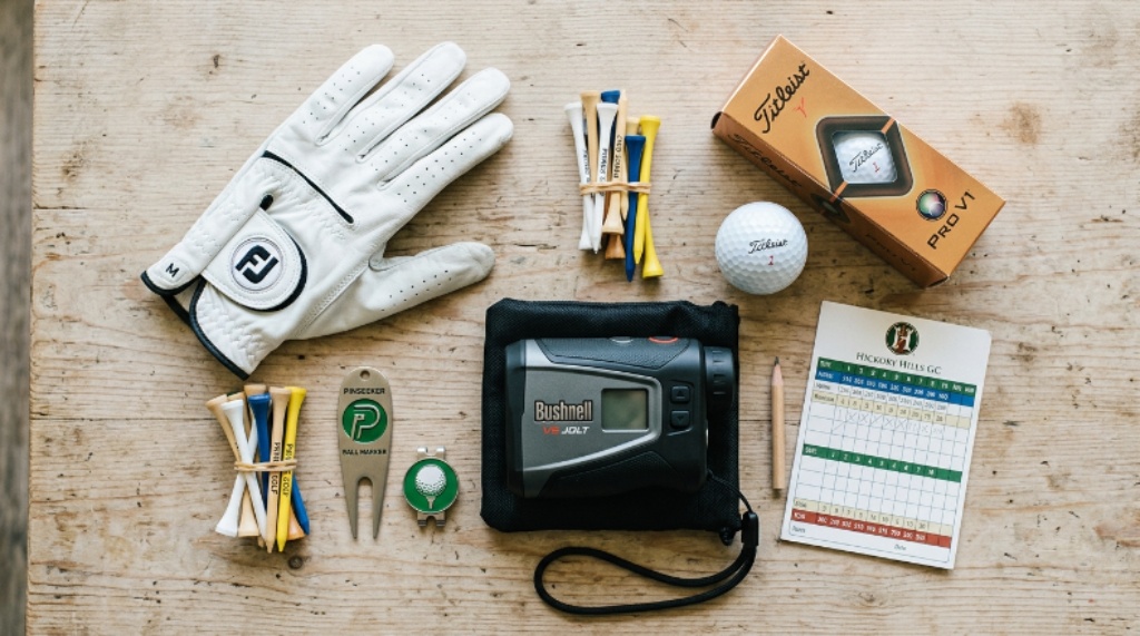 Flat lay of essential beginner golf equipment including a golf glove, tees, divot tool, ball marker, and rangefinder